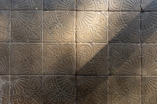 Vintage concrete floor tile pavement featuring traditional embossed floral patterns under high contrast bright natural sunlight and sharp shadow details, perfect for rustic abstract texture background