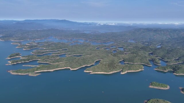 Drone footage captured over Ta Dung Lake in Dak Nong Province, Vietnam, at sunrise. Filmed from very high altitude, the drone gradually pulls back to reveal the full expanse of the reservoir, forested
