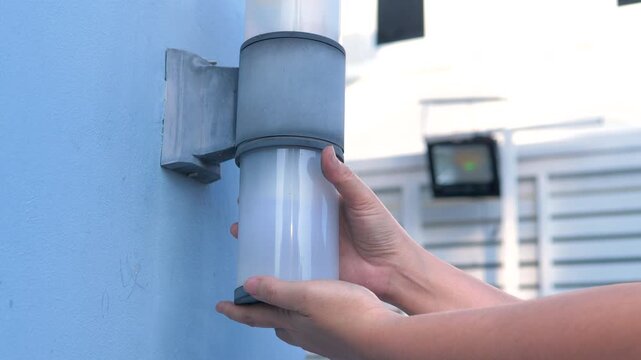 Close up shot of a person hand replacing or installing an energy-saving LED light bulb into an outdoor wall lamp fixture of a residential building