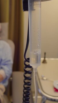 Medical infusion equipment and female patient during treatment session in healthcare facility, rack focus highlighting connection between clinical care, healing and recovery