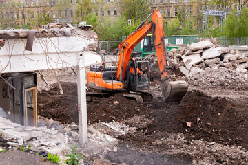 Fototapeta premium Orange excavator working on demolition site clearing concrete debris and rubble.