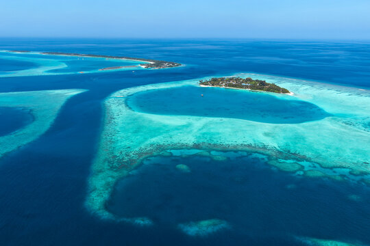 Aerial view of the tropical island of Vaanee surrounded by vibrant turquoise lagoon waters, coral reefs, and deep blue ocean in Vaanee, Dhaalu Atoll, Maldives.