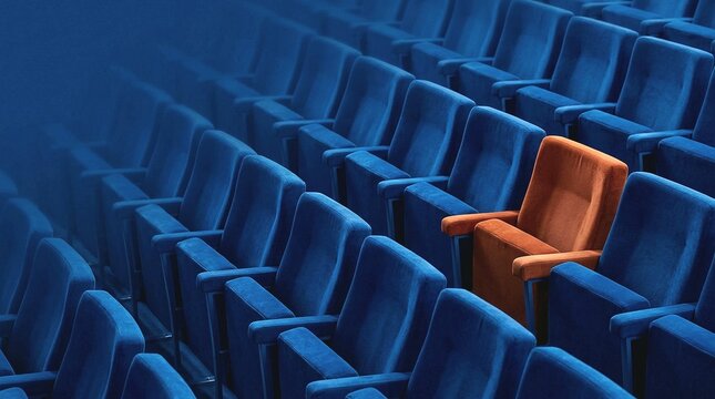 An orange seat stands out among many blue empty seats in an auditorium symbolizing individuality and uniqueness