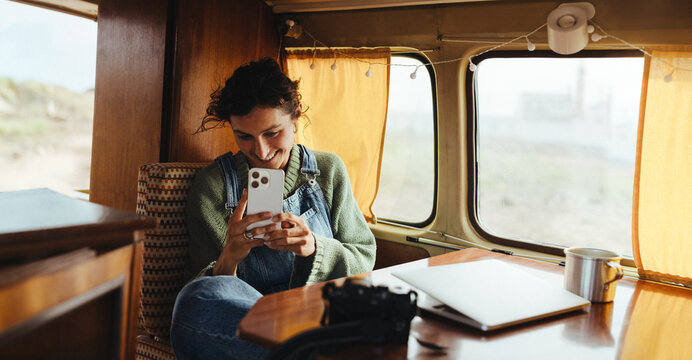 Woman on a cozy road trip bus using smartphone, relaxing with laptop and coffee nearby