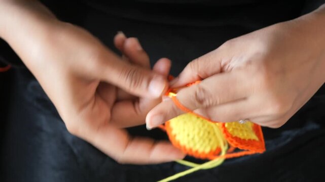 Crochet enthusiast hands stitching colorful yellow and orange wool yarn creating handmade fabric artwork