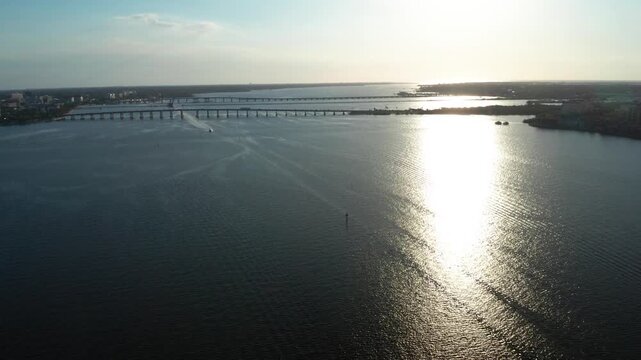 Rippling Manatee River water reflects a bright sun path as a small boat heads toward long parallel bridges in the distance.