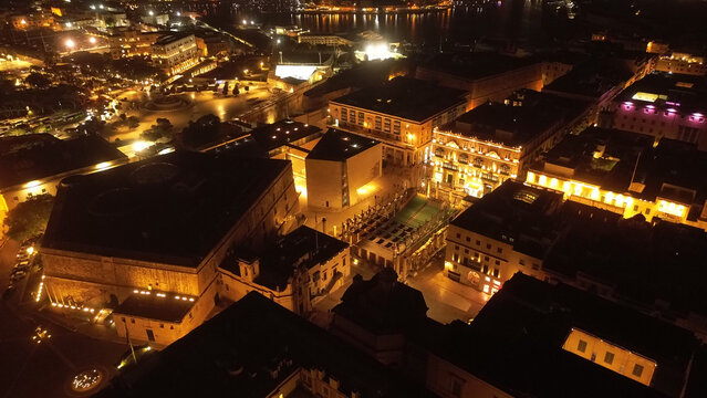 Aerial view of the illuminated historic city center of Valletta at night, featuring the Parliament Building and City Gate area with glowing streetlights in Valletta, Port Region, Malta.