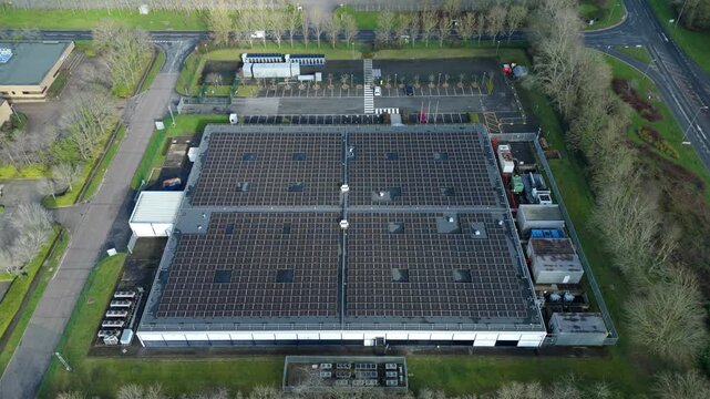 High-angle aerial drone shot of a state-of-the-art data centre in Milton Keynes, UK. Features large rooftop solar panels powering modern infrastructure dedicated to quantum computing technology and AI