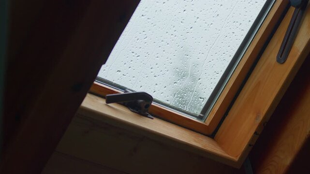 Raindrops skylight window, static tripod shot. Close up detail of rain droplets streaming down glass pane of wooden attic window during storm.
