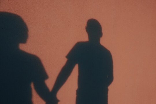Shadow silhouettes of a couple holding hands on a textured beige wall