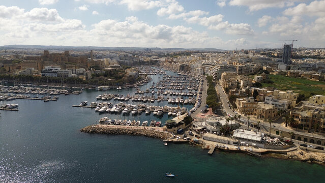 Aerial view of the Msida Marina with numerous yachts and boats docked in the harbor, surrounded by urban architecture and coastal roads in Valletta, Port Region, Malta.