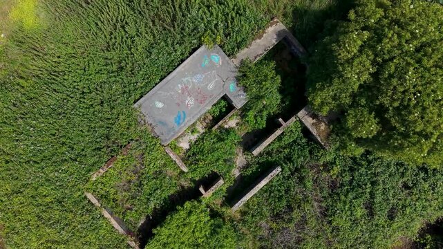 Chadwell Heath ZE1 gun emplacements seen from above as drone flies forward over overgrown WWII anti-aircraft battery remains, concrete hardstands and structures in east London, UK.