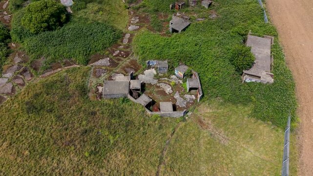 Chadwell Heath ZE1 gun emplacements seen from above as drone reverses and rises, revealing octagonal concrete AA battery remains, overgrown grassland, WWII heritage landmark in London, UK.