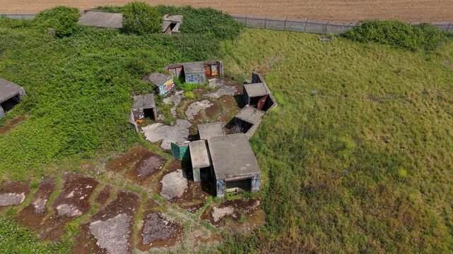 Gun Emplacements ZE1 ruins in Chadwell Heath, London. Drone descends over derelict concrete WWII anti-aircraft battery with overgrown scrub, graffiti and bunkers.