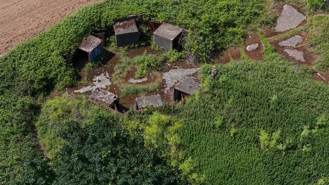 ZE1 gun emplacement ruins in Chadwell Heath, England, aerial orbit around six circular AA battery buildings amid overgrown scrub and concrete pads, WWII heritage military site.