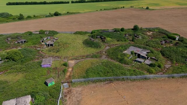 ZE1 gun emplacements, Chadwell Heath aerial orbit showing WWII anti-aircraft battery concrete bunkers, magazine huts and access paths amid overgrown grassland on former RAF London defences site.