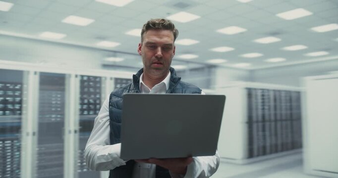 360 Degree. Caucasian Male It Engineer Holds Laptop, Analyzing Server Data and Optimizing Network Infrastructure in Data Center. Tech Professional Inspects Systems. Orbital Cinematic Arc Tracking Shot