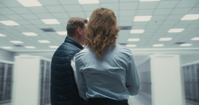 360 Degree. Male and Female Technicians Discuss AI Software on Laptop While Examining Server Racks in a Data Center, Planning Network Maintenance and Performance Optimization. Orbital Cinematic Arc