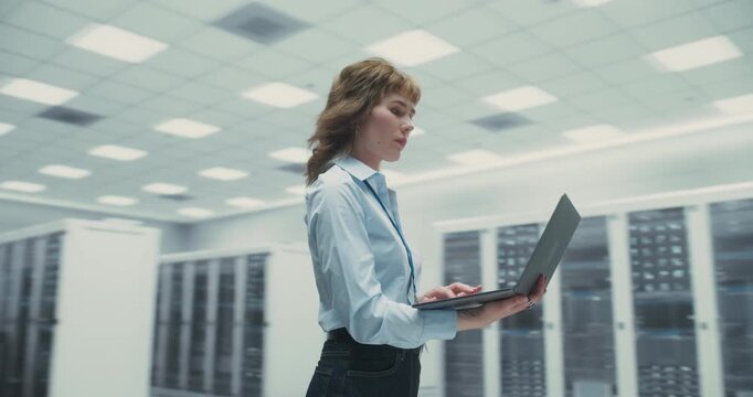 360 Degree. Female Specialist Holds Laptop While Inspecting AI Server Racks in a Data Center, Reviewing Cloud Network Data and Improving Digital System Performance. Orbital Cinematic Arc Tracking Shot