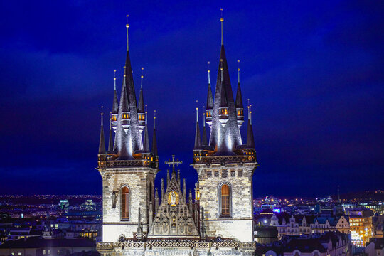 Aerial view of the Church of Our Lady before Tyn with its iconic gothic spires illuminated at night, overlooking the historic city skyline of Prague, Prague, Czechia.
