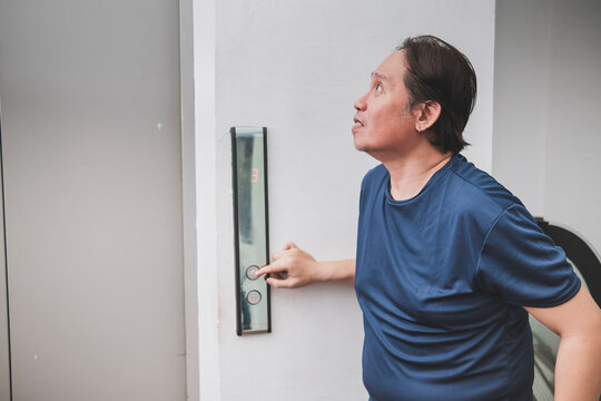 Southeast Asian man anxiously waits for an elevator, appearing uncomfortable and eager to reach his destination quickly.