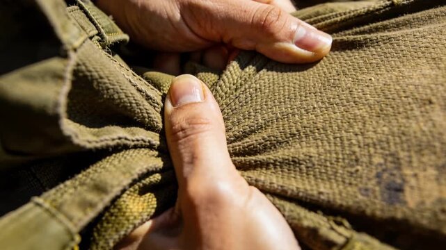 Bringing hands together, adult pinching and checking olive-green canvas in sunlight, showing watch