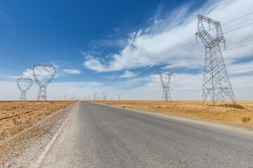 Obraz premium Desert Highway Flanked by High-Voltage Transmission Towers Under Expansive Blue Sky