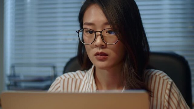 Woman wearing glasses working on laptop at night.
