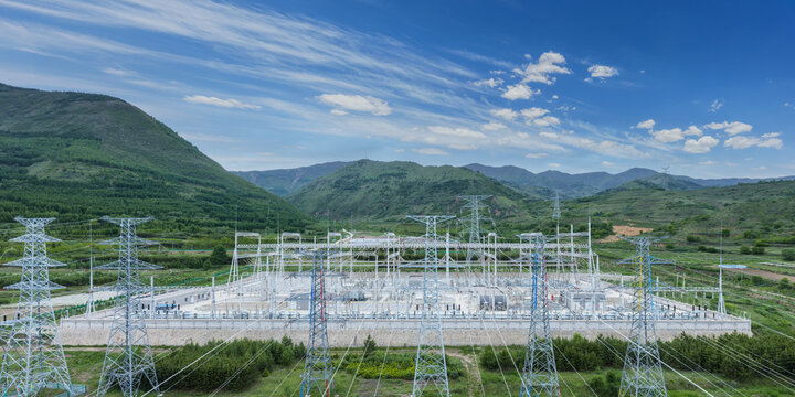 High-Voltage Substation Nestled in Green Mountain Valley Under Bright Blue Sky