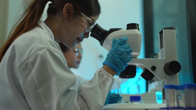 Team of biochemical research scientists working with a microscope for vaccine development in pharmaceutical research labeling.