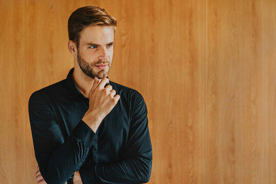 Serious young and ambitious businessman, project leader dressed in formal wear posing in modern workspace, exuding leadership, competence, experience, and professionalism. Corporate portrait