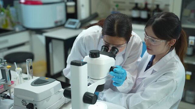 Team of biochemical research scientists working with a microscope for vaccine development in pharmaceutical research labeling.