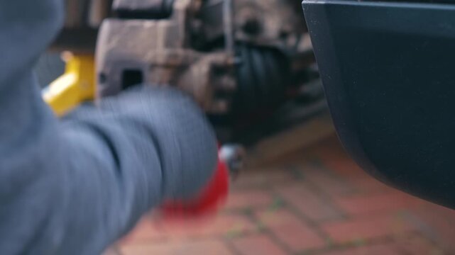 Removing brake caliper slider bolt with socket wrench during vehicle brake repair procedure. Automotive maintenance concept with disc brake component disassembly, exposed caliper mechanism and