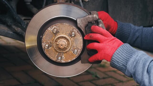 Servicing brake caliper on car disc brake assembly. Repairing vehicle braking system with hands adjusting caliper components during maintenance outdoors. Automotive mechanical repair focusing on brake