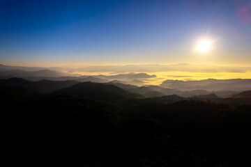 Fototapeta premium Beautiful aerial view of bright foggy morning over dark hills with mountain forest trees.