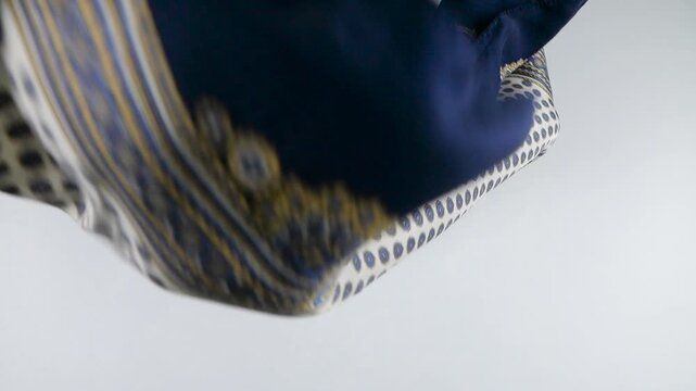 Luxury silk scarf with a paisley pattern in navy blue and beige falls in slow motion onto a white background. Clean commercial stock footage showcasing high-quality textile details for fashion.