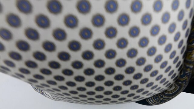 Navy blue and beige luxury silk scarf with a paisley pattern falls in slow motion onto a white background. Clean commercial stock footage showcasing high-quality textile details for fashion.