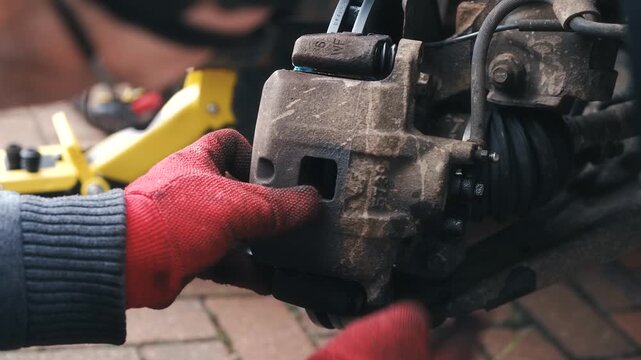 Automotive technician installing brake caliper onto vehicle during repair. Close up mechanical assembly with gloved hands positioning caliper over brake disc and pad components. Car brake system