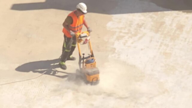 Moscow, June 20 2026, Worker in orange vest and white helmet pushes dust suppressant machine.\nMachine sprays fine mist to control dust on construction site.\nDust clouds form as the worker moves acro