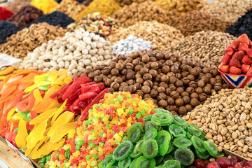 Fototapeta premium Vibrant trays of dried mango, kiwi, pineapple, and almonds at a Central Asian bazaar. Concept: Oriental market abundance and culinary tourism in Asia