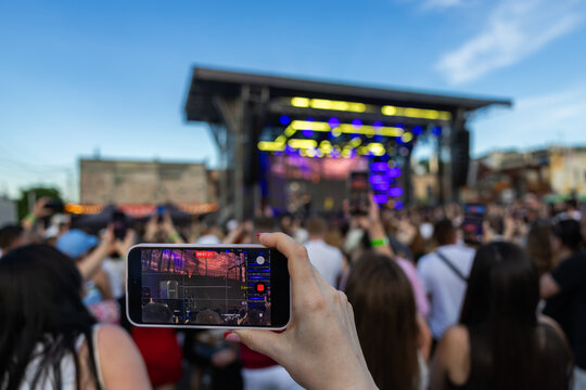 Hand holding smartphone recording video of live concert music festival stage