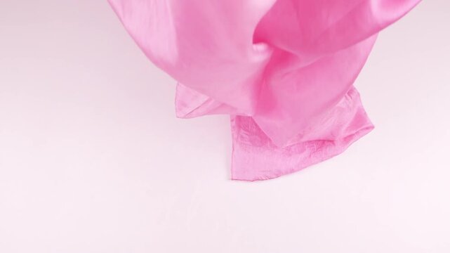 Fuchsia pink silk fabric falls smoothly onto a white background in slow motion. Elegant lightweight textile creates soft waves and delicate folds for luxury fashion and cosmetics brand advertising.