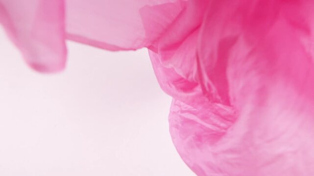 Fuchsia pink silk scarf falls onto a white background in slow motion. Texturized fabric creates organic movement and gentle folds for luxury fashion, textile industry, and cosmetic advertising.