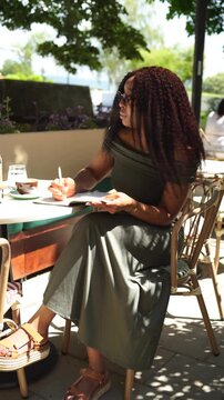 Young woman in a cafe outdoors writing in a notebook on a sunny day