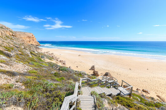 Wooden boardwalk winding through the rugged coastal landscape of Innes National Park, overlooking the sandy shores and deep blue ocean of Ethel Wreck Beach on a bright summer day, Yorke Peninsula, SA