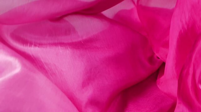 Pink silk scarf falls onto a white background in slow motion. Luxury fabric creates elegant folds for fashion industry concepts and commercial cosmetic advertising.