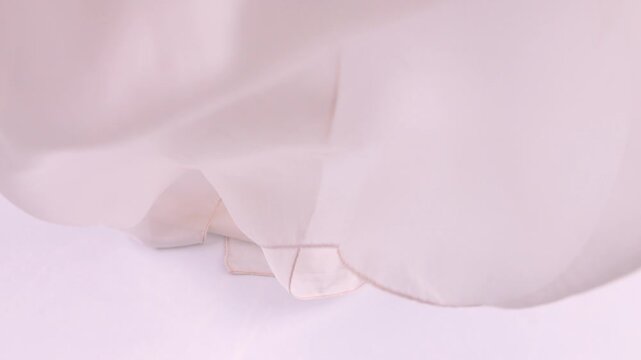 Pink silk fabric falls onto a white background in slow motion. Soft folds create luxury textures for fashion and beauty commercials. Delicate rose textile drapes to form a romantic background.
