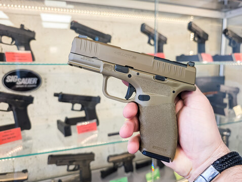 BALTIC STATES - JUNE 22, 2026: A customer in a gun shop holds and inspects a Springfield Armory Hellcat Pro OSP FDE 9mm pistol against a showcase display.
