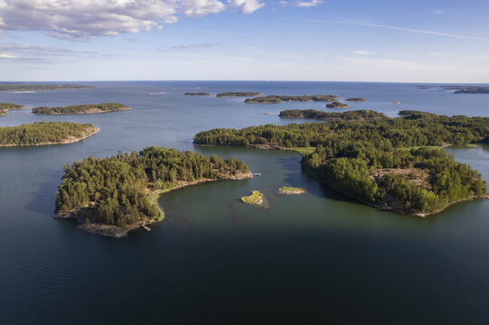Aerial view of the Espoo archipelago with lush green islands, rocky shorelines, and calm blue waters under a clear sky in Espoo, Uusimaa, Finland.