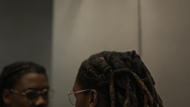 Tilt down shot of young Black man with dreadlocks looking at reflection in mirror in front of surveillance cameras. ideal for mental health awareness, corporate stress, or self-reflection concept